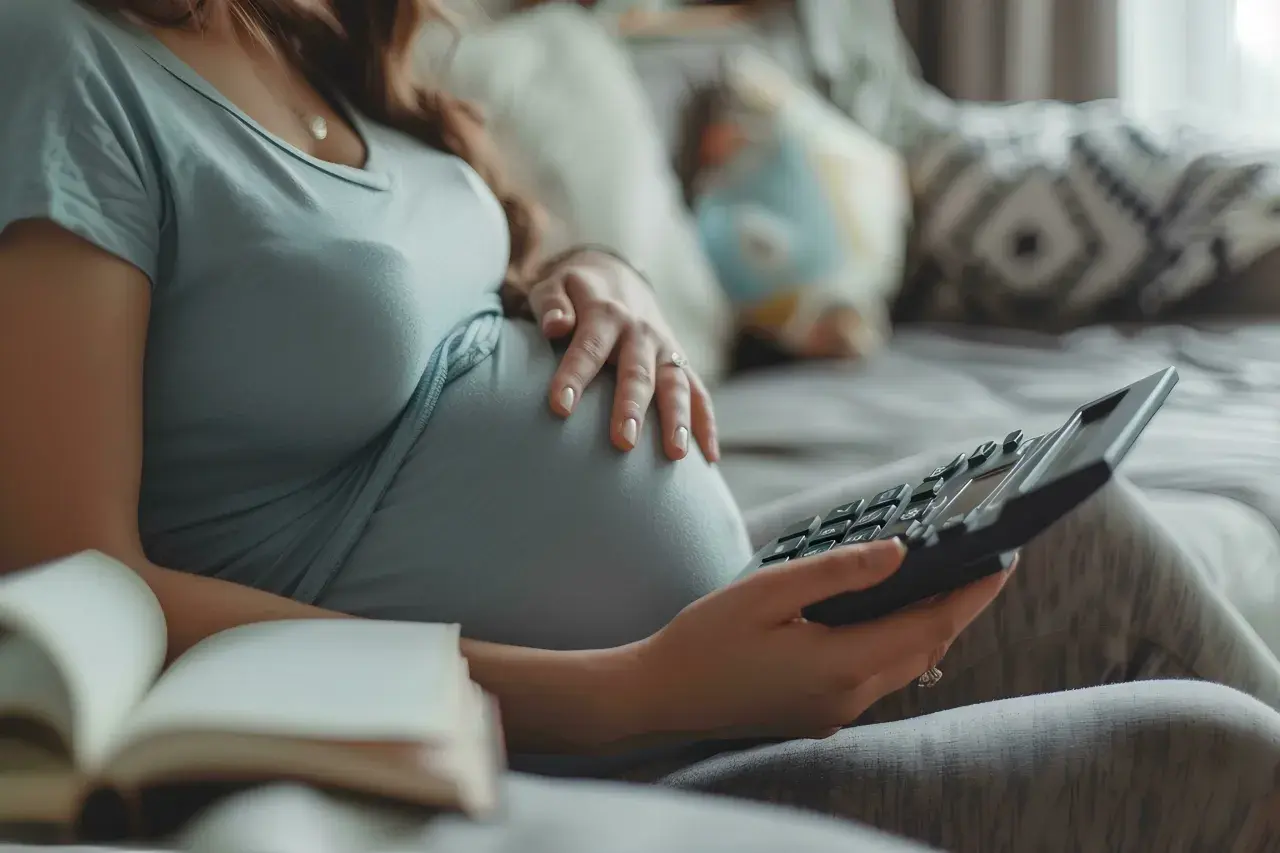 Ciężarna kobieta z kalkulatorem i otwartą książką na kanapie.