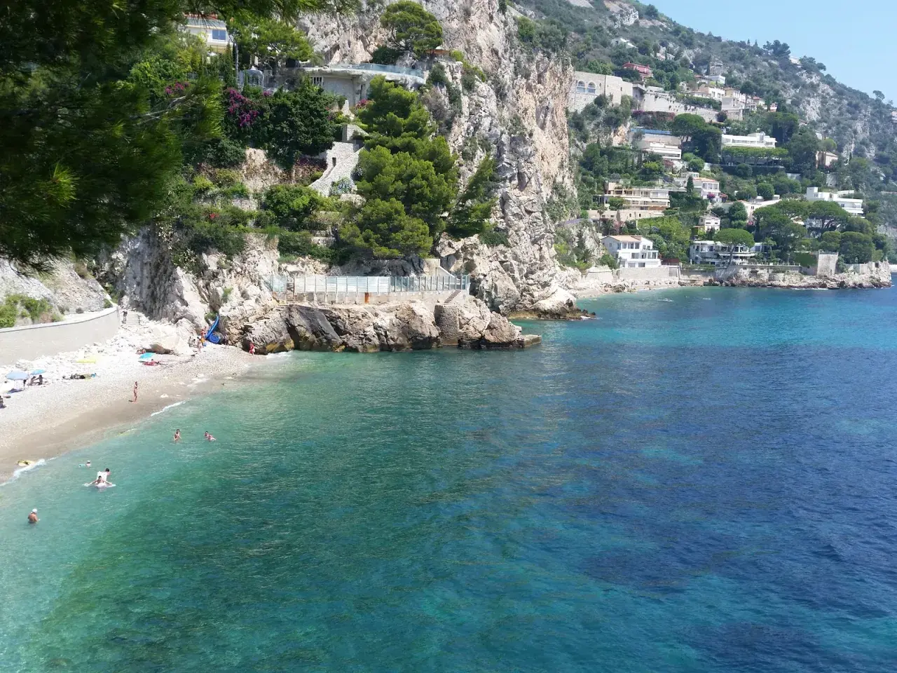 Spiaggia di Eze-sur-Mer con ville aggrappate alla scogliera e acque turchesi cristalline.