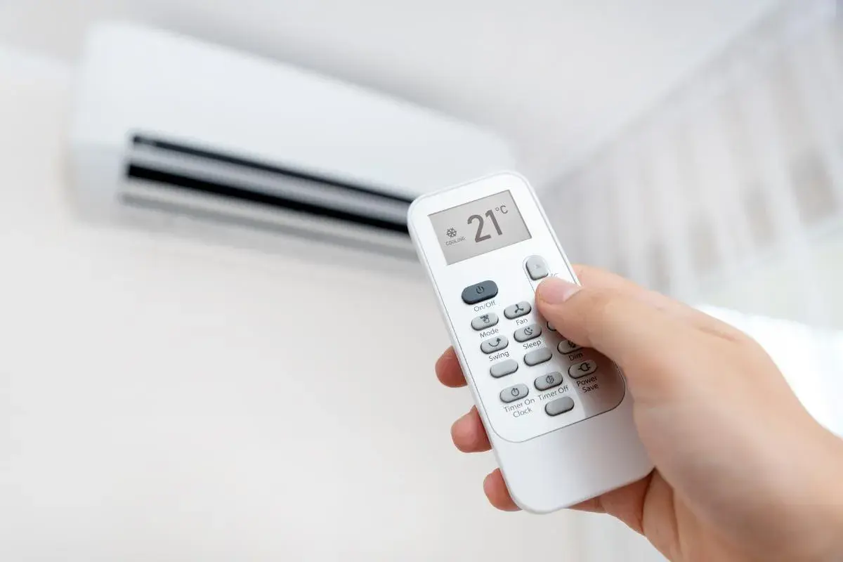 Mano ajustando el control remoto del aire acondicionado a 21°C en modo cooling. Perfecto para el heat cool en español.