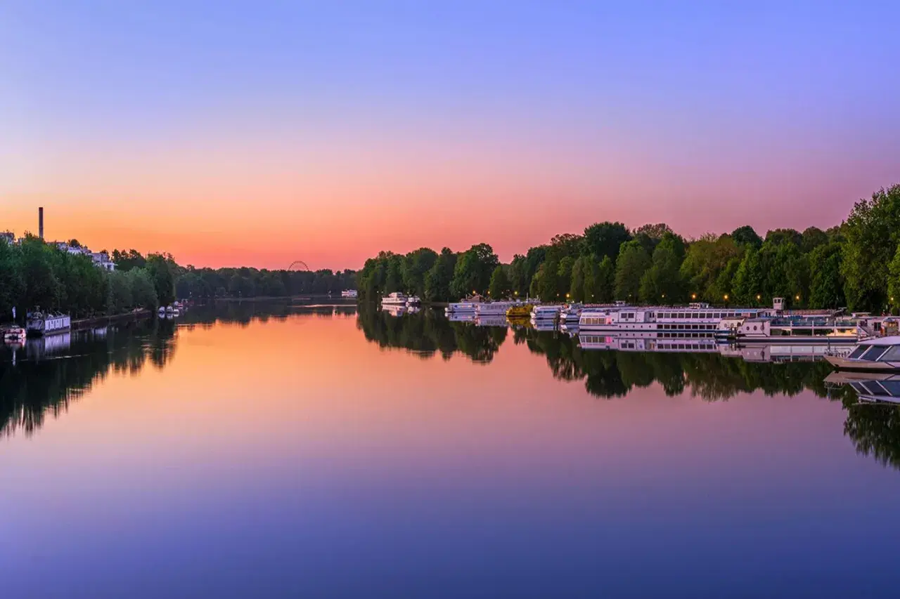 Boote liegen im Wasser vor dem grünen Ufer des Treptower Parks im Abendrot.