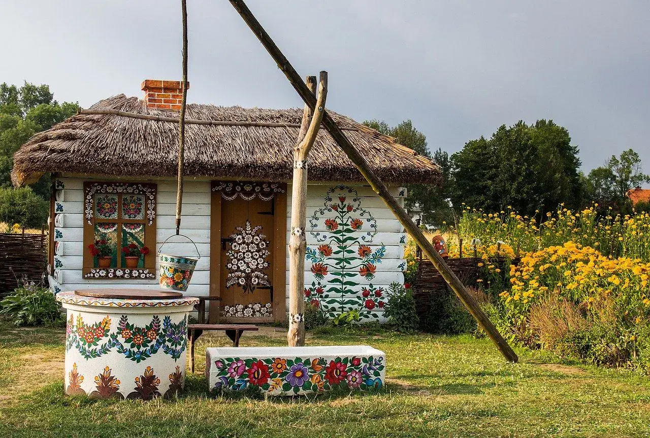 Kolorowy dom z malowanymi kwiatami, studnia i ławka. Zalipie atrakcje zachwycają ludowym pięknem.