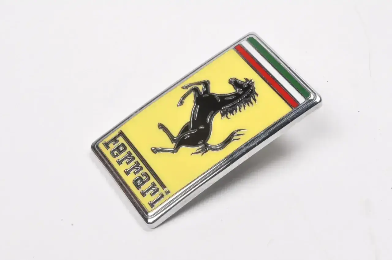 Oto jak wygląda znaczek Ferrari: czarny koń na żółtym tle, z napisem "ferrari" i włoską flagą.