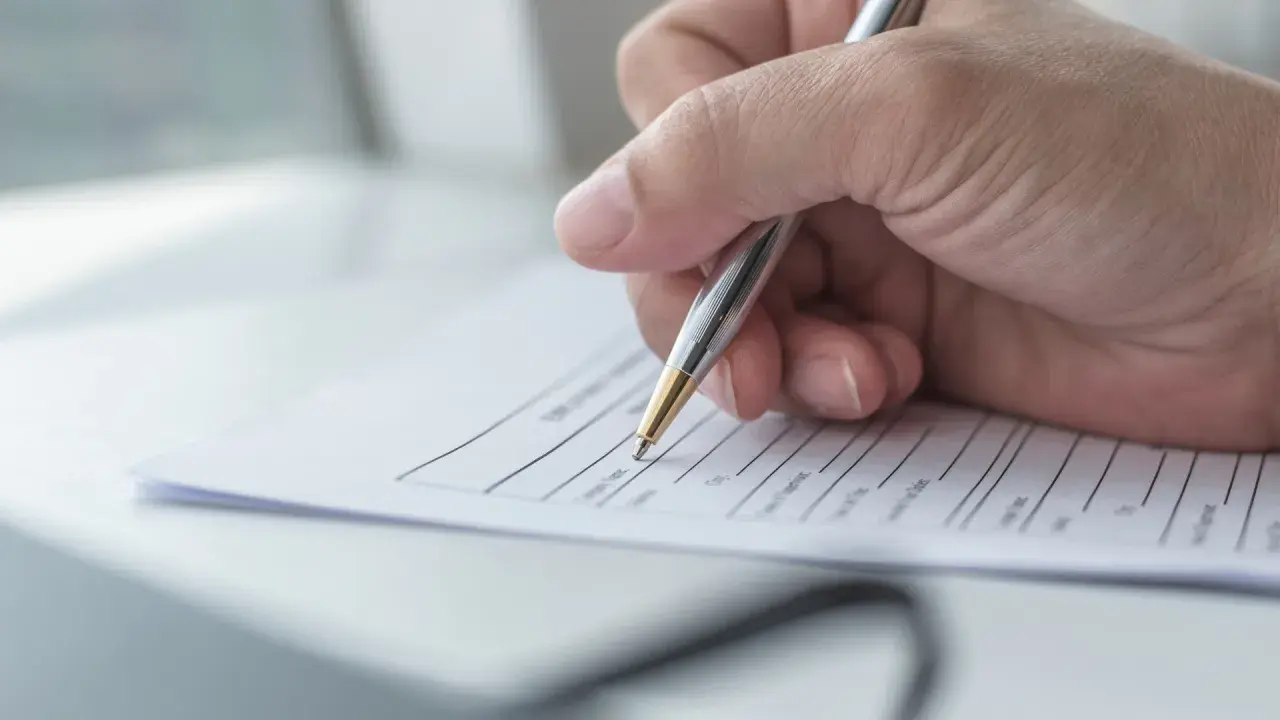 Dłoń pisze długopisem na kwestionariuszu osobowym dla pracownika.