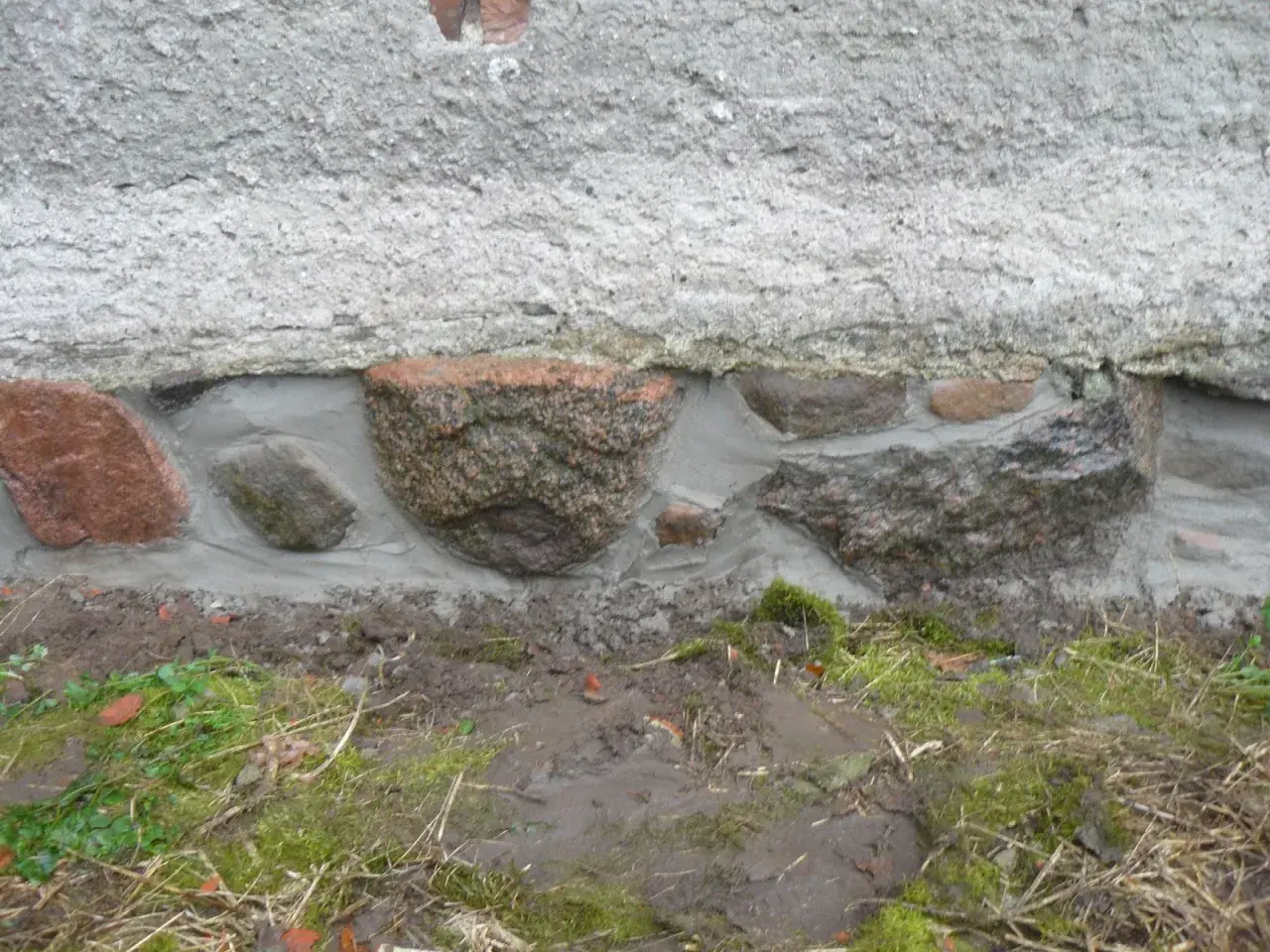 Das Feldsteinfundament wird mit Mörtel abgedichtet. Große Steine sind sichtbar, umgeben von frischem Mörtel, der die Lücken füllt.