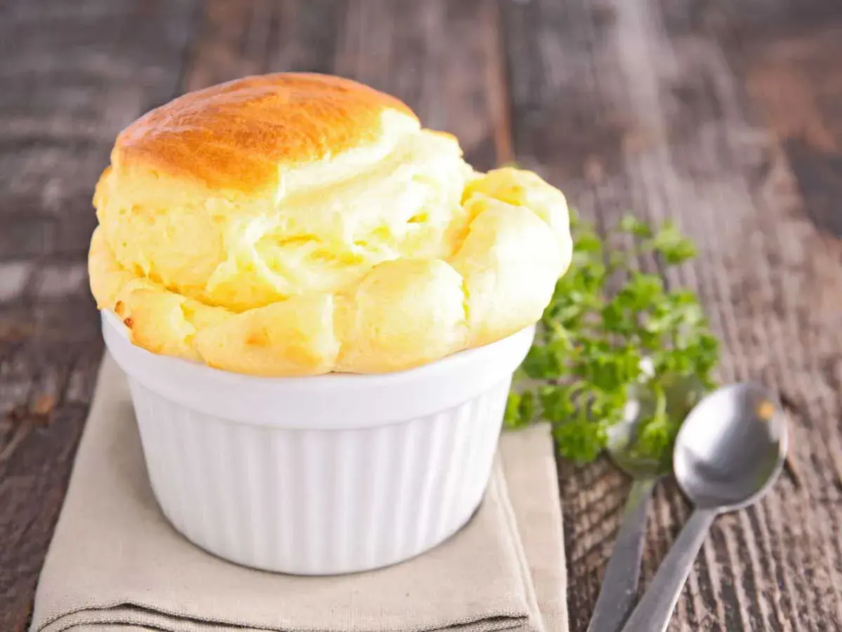 Un délicieux soufflé au fromage, doré et gonflé, servi dans un ramequin blanc sur une table en bois rustique.