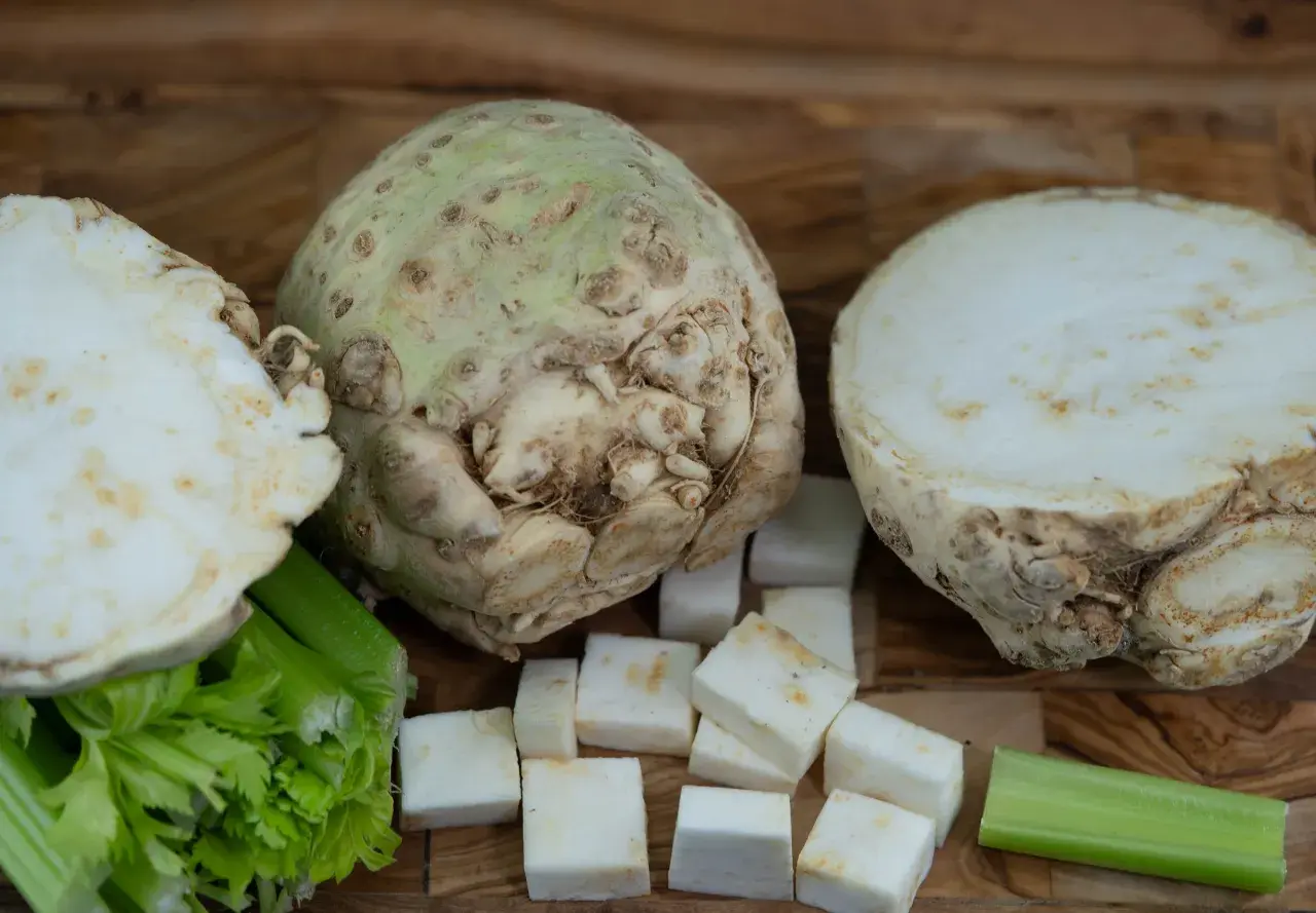 Knollensellerie-Rezepte für eine herzhafte Hauptspeise: Ein ganzer Knollensellerie, halbiert und gewürfelt, mit Staudensellerie auf Holzuntergrund.