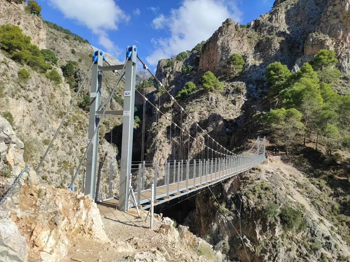Puente colgante en la ruta del saltillo, con imponentes montañas rocosas y vegetación verde.
