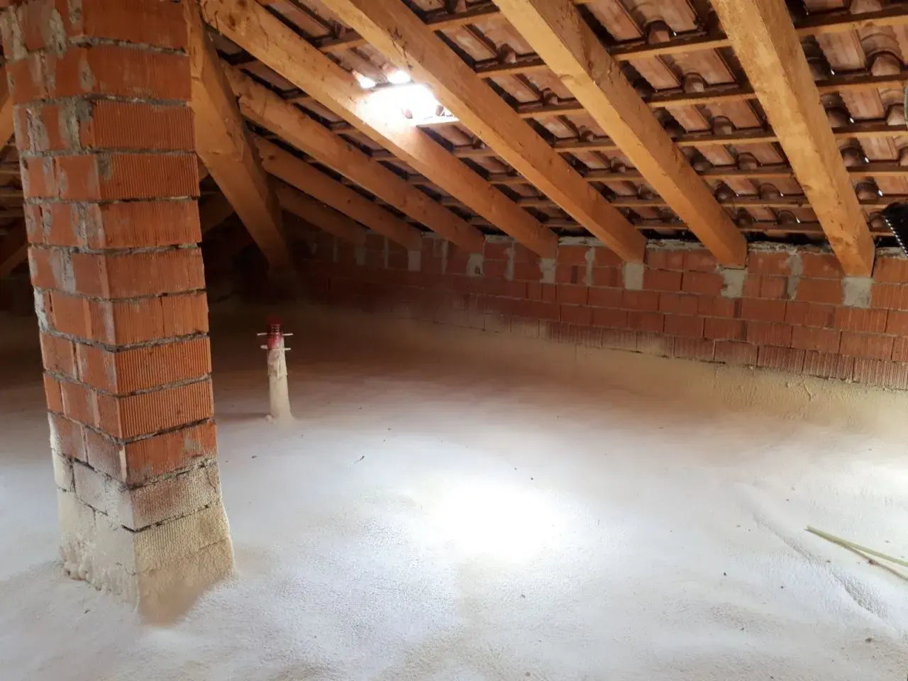 Sottotetto in fase di isolamento con schiuma espansa. Si vede la struttura in legno e mattoni, segno che conviene isolare il sottotetto per un maggiore comfort.