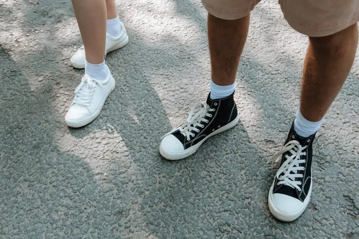 Białe i czarne trampki, idealne buty na długie marsze, stoją na szarej nawierzchni.