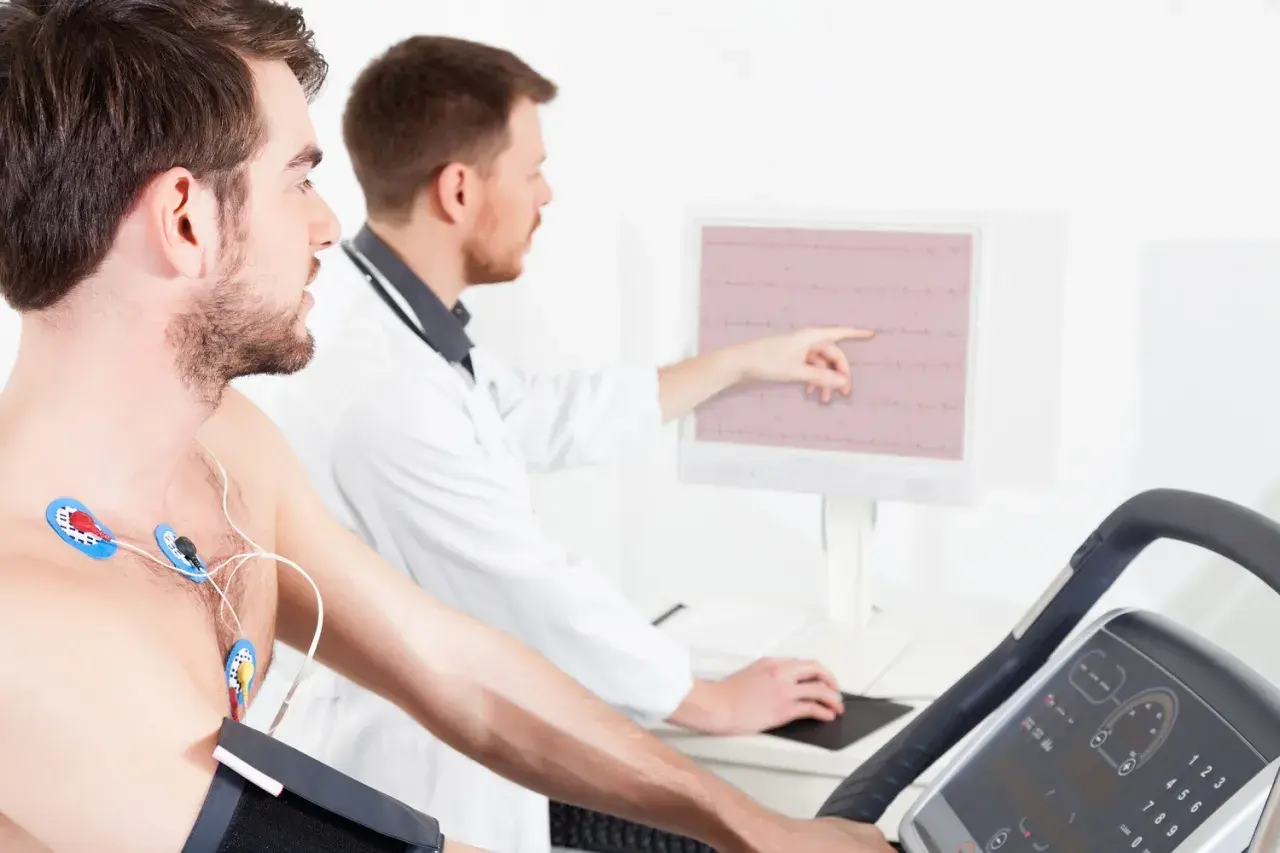 Un homme subit un test d'effort dangereux sur un tapis roulant, des électrodes sur la poitrine, tandis qu'un médecin surveille son rythme cardiaque sur un écran.