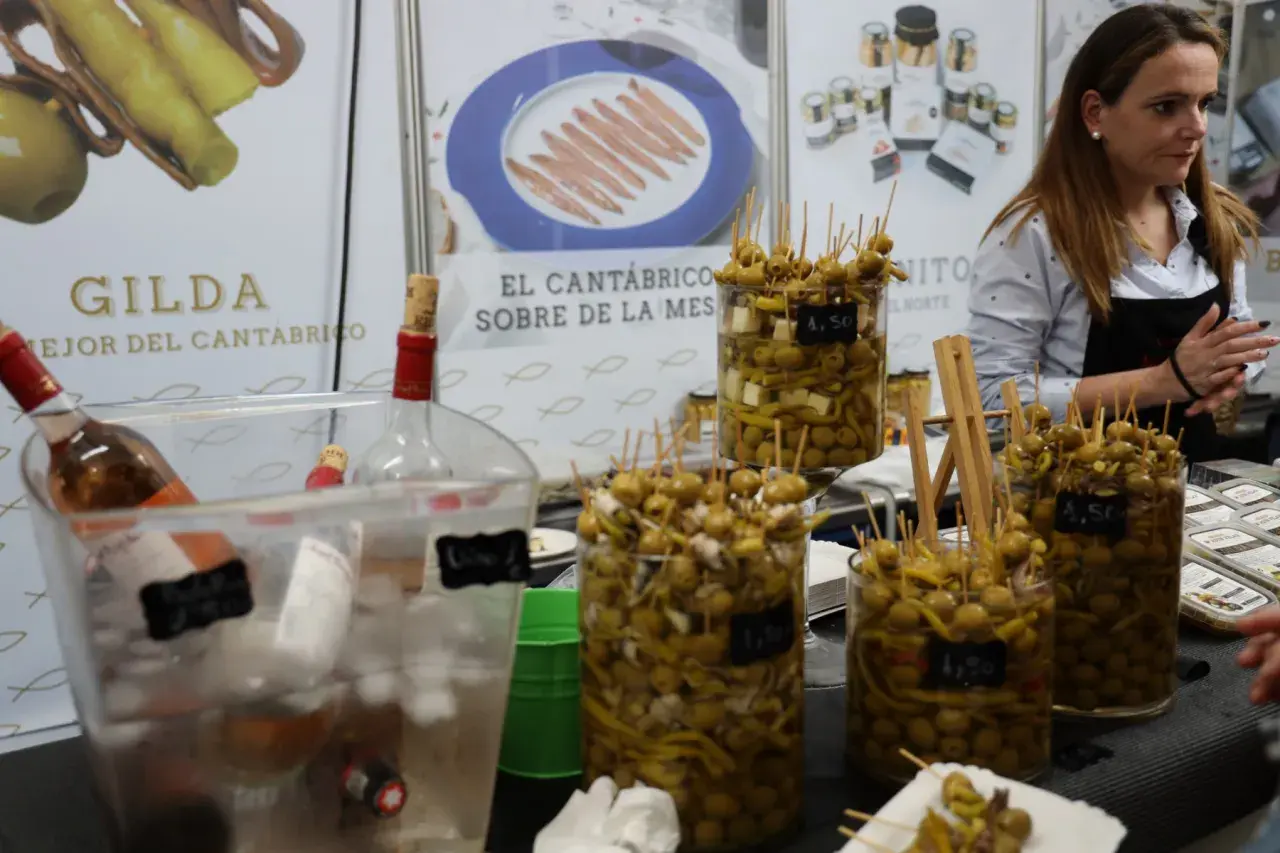 En la feria de la anchoa en Santoña, se exhiben gildas y aceitunas marinadas. Botellas de vino esperan ser servidas.