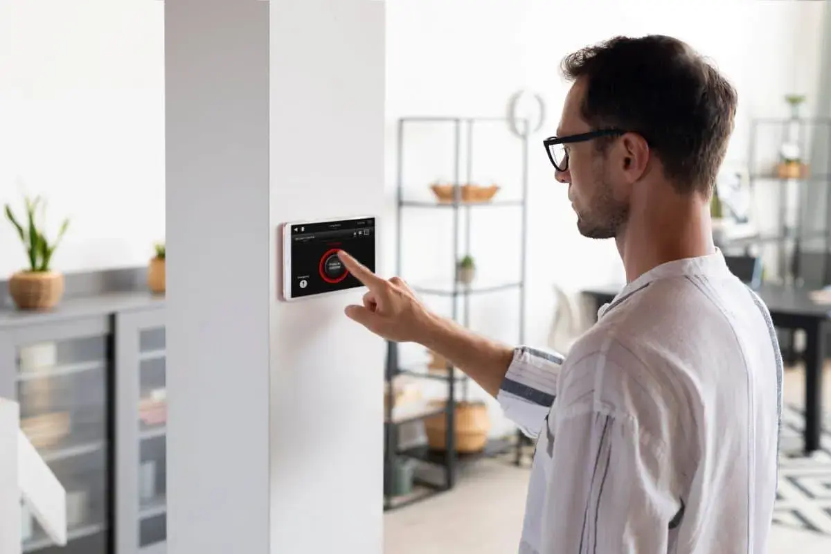 Hombre interactúa con pantalla táctil de domótica, controlando luces y seguridad. Los sensores domotica hacen el hogar inteligente.