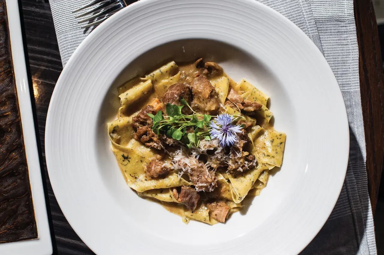 En tallrik med breda bandnudlar, möra bitar av oxfilé och en krämig sås, toppad med färska örter och en blå blomma. En utsökt oxfilé pasta.