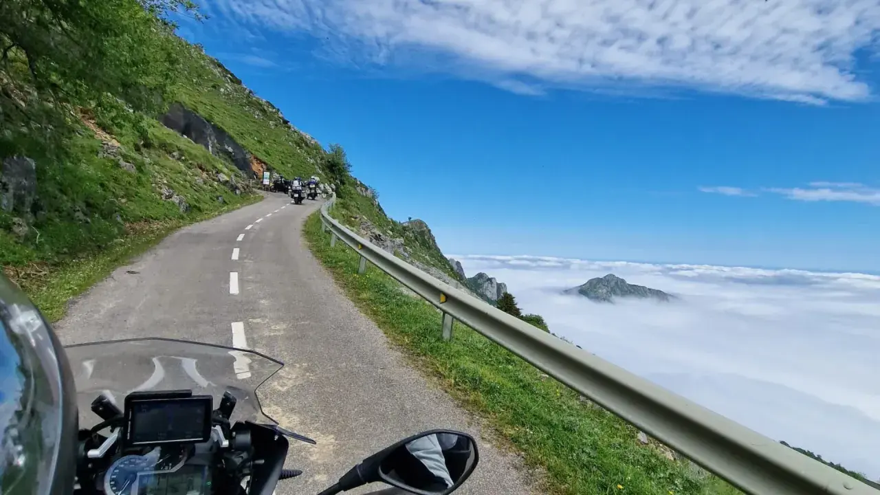 Motociclistas en un viaje por carretera, con un paisaje montañoso y nubes. El significado de este trip km es la aventura.