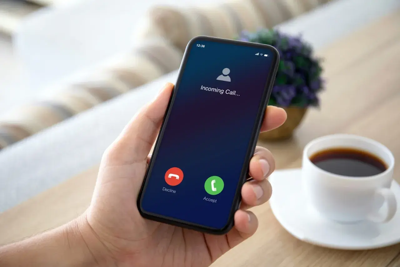 Dłoń trzyma smartfon z ekranem połączenia przychodzącego.