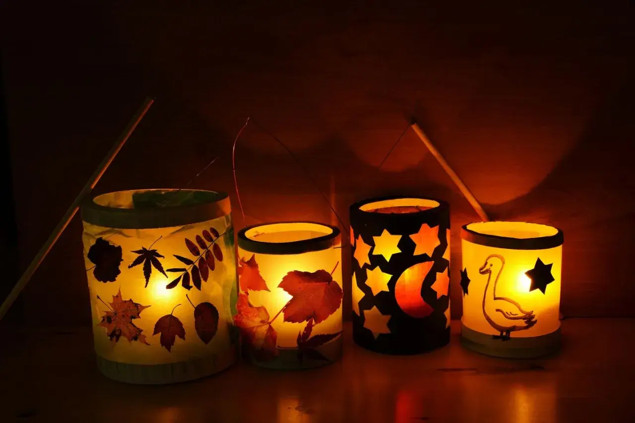 Vier selbstgebastelte Tischlaternen für Kinder leuchten warm. Mit Blättern, Sternen, Mond und einem Gänse-Motiv.