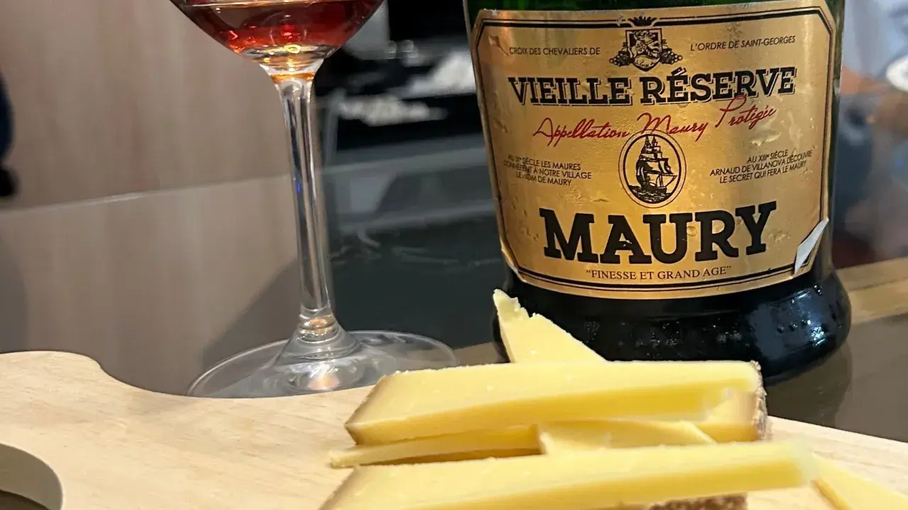 Verre de vin et fromage sur planche en bois, à côté d'une bouteille de Maury. La question est : que boire avec du fromage ?