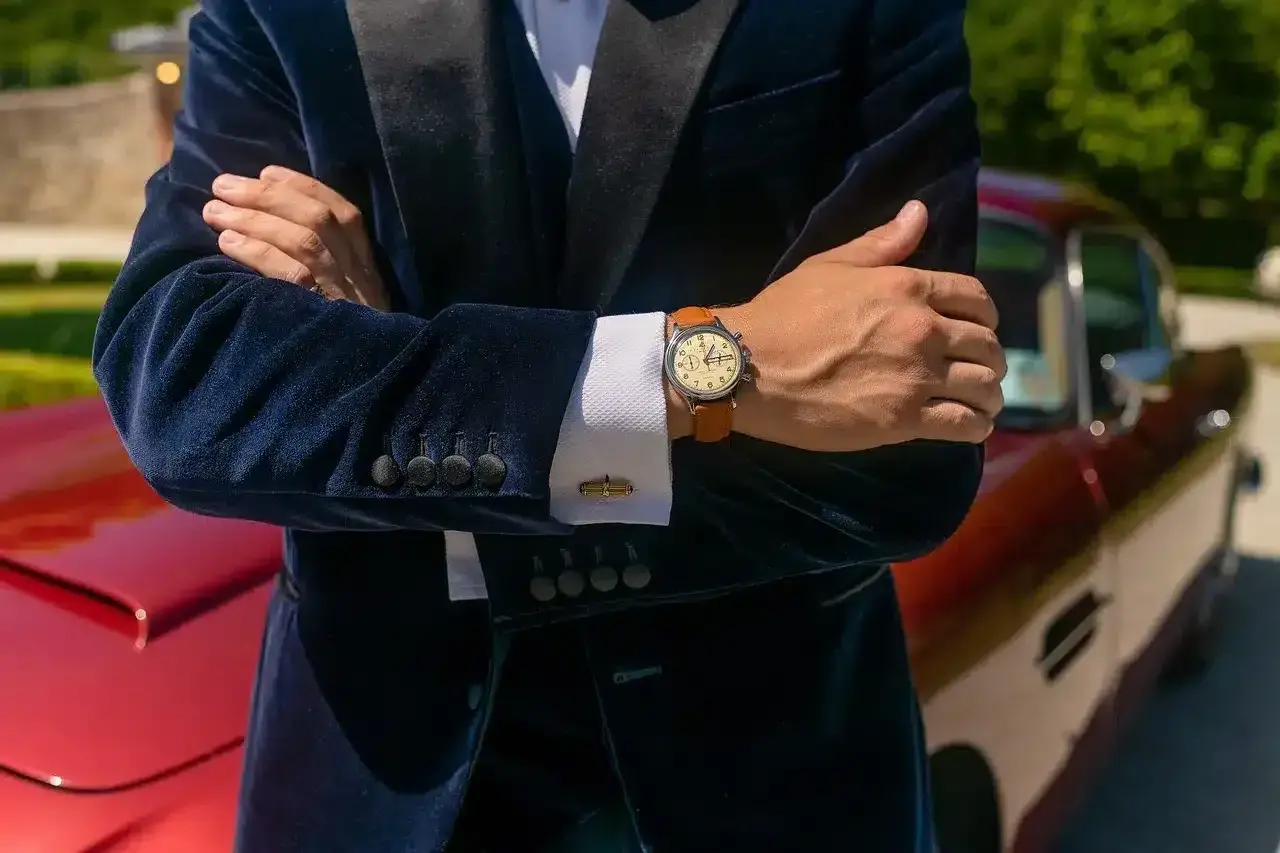 Elegancki mężczyzna w granatowym aksamitnym garniturze i białej koszuli pokazuje, jak nosić zegarek do koszuli. Klasyczny styl.