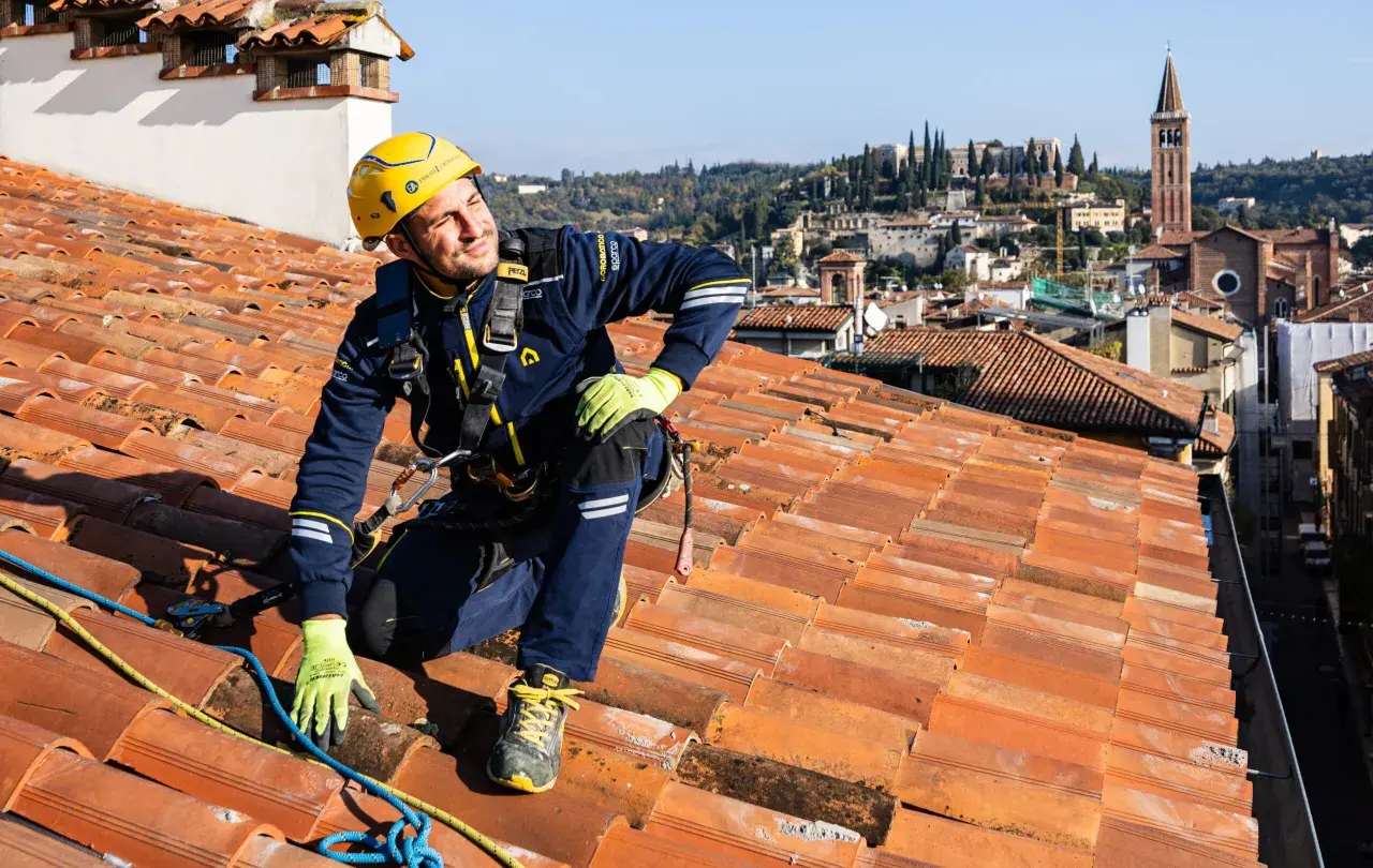 Operaio in corda per la riparazione tetto casa, con vista panoramica sulla città.