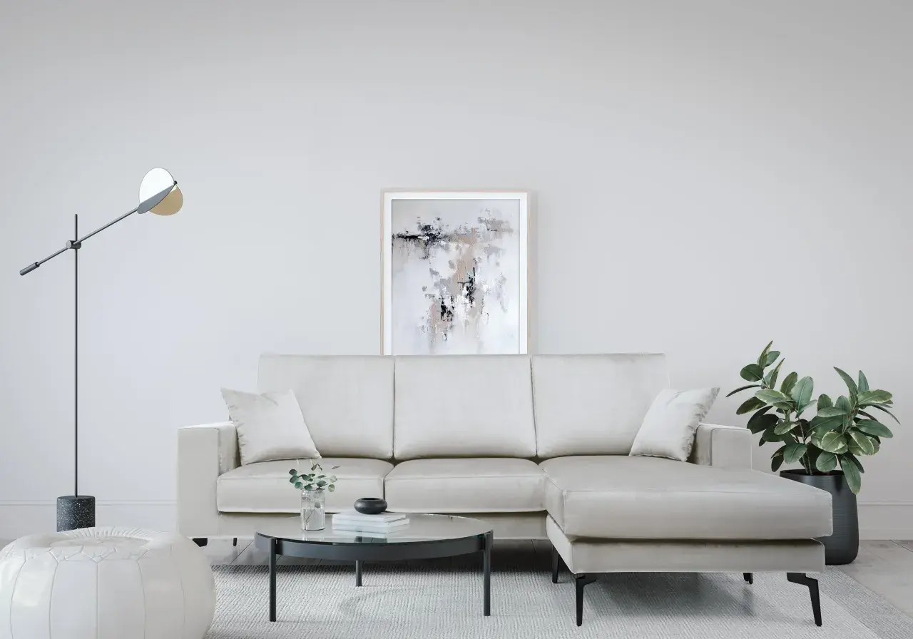 Divano angolare color crema, con tavolino rotondo in vetro, pouf bianco e quadro astratto. Le misure divano angolare sono perfette per questo spazio.
