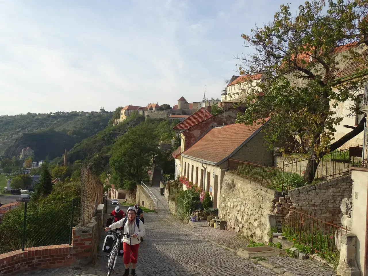 Radfahrer erkunden eine Kopfsteinpflasterstraße in Znaim, Tschechien, mit historischen Gebäuden und einer Burgruine im Hintergrund.