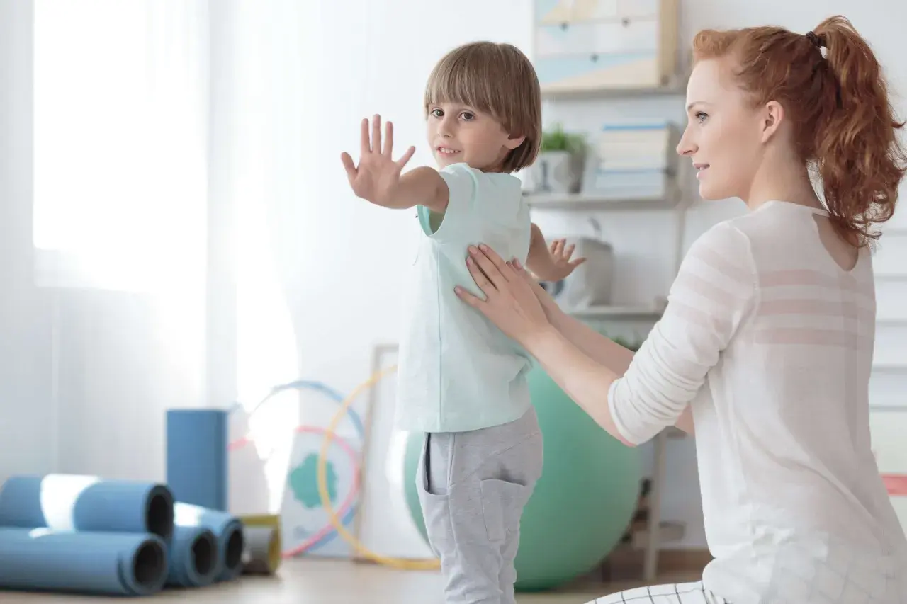 Ein Kind mit Skoliose erhält osteopathische Behandlung. Eine Therapeutin legt sanft die Hände auf den Rücken des Jungen, der sich leicht wegdreht.