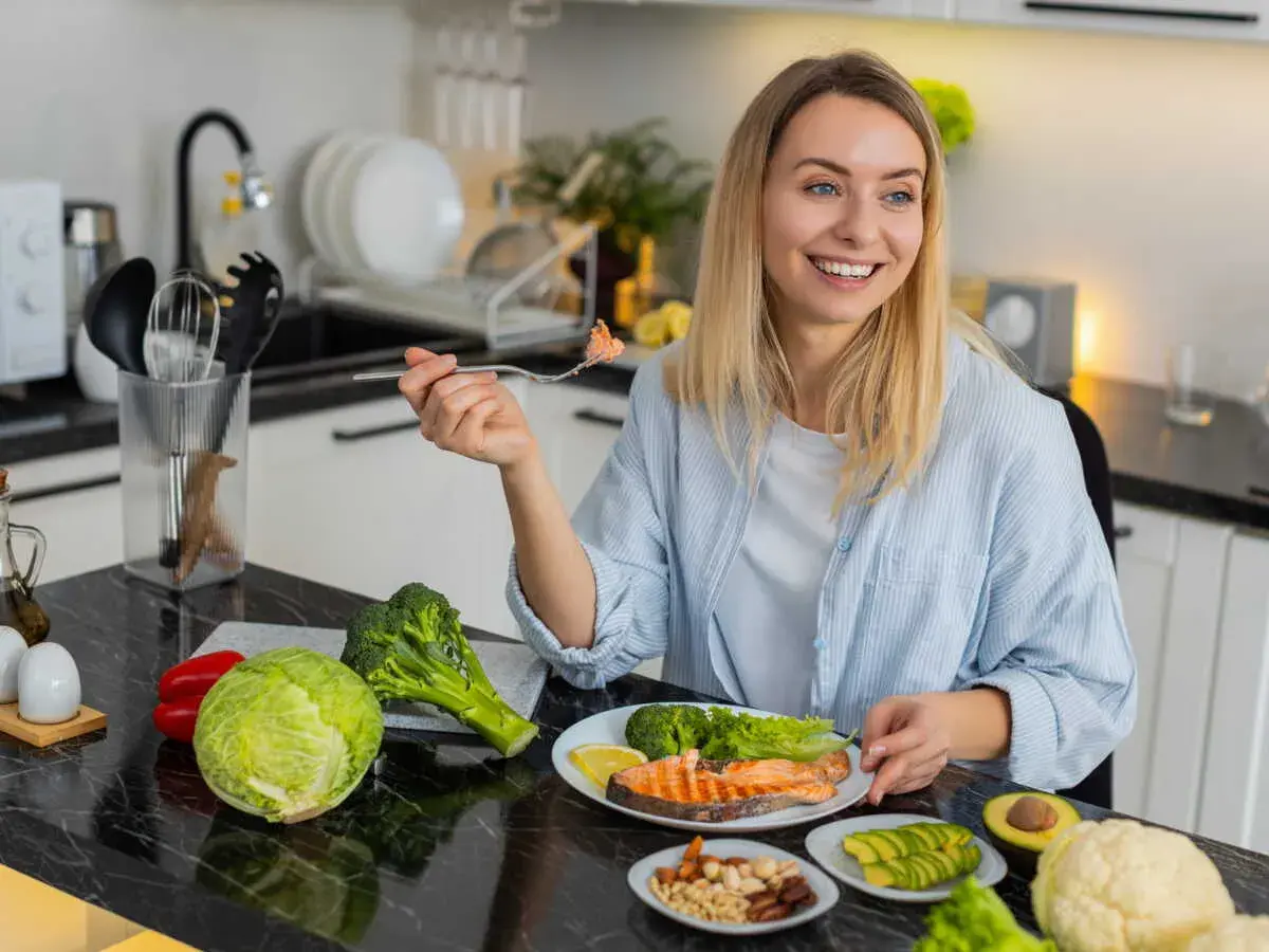 Femme souriante dégustant un menu équilibré pour perdre du poids : saumon, brocolis, avocat, noix et légumes frais.