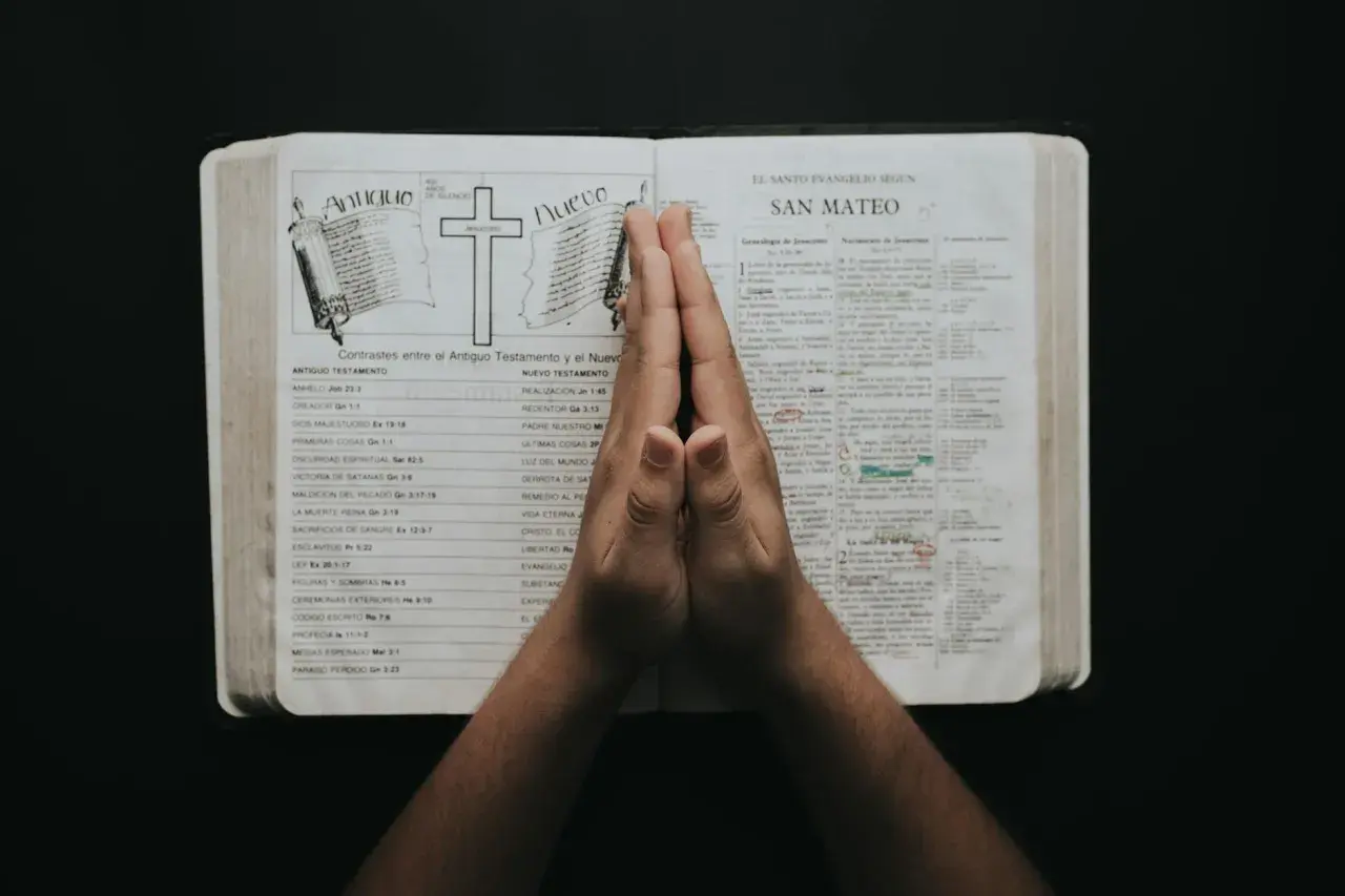 Dłonie złożone do modlitwy na otwartej Biblii. To inspiracja na modlitwa na każdy dzień tygodnia.