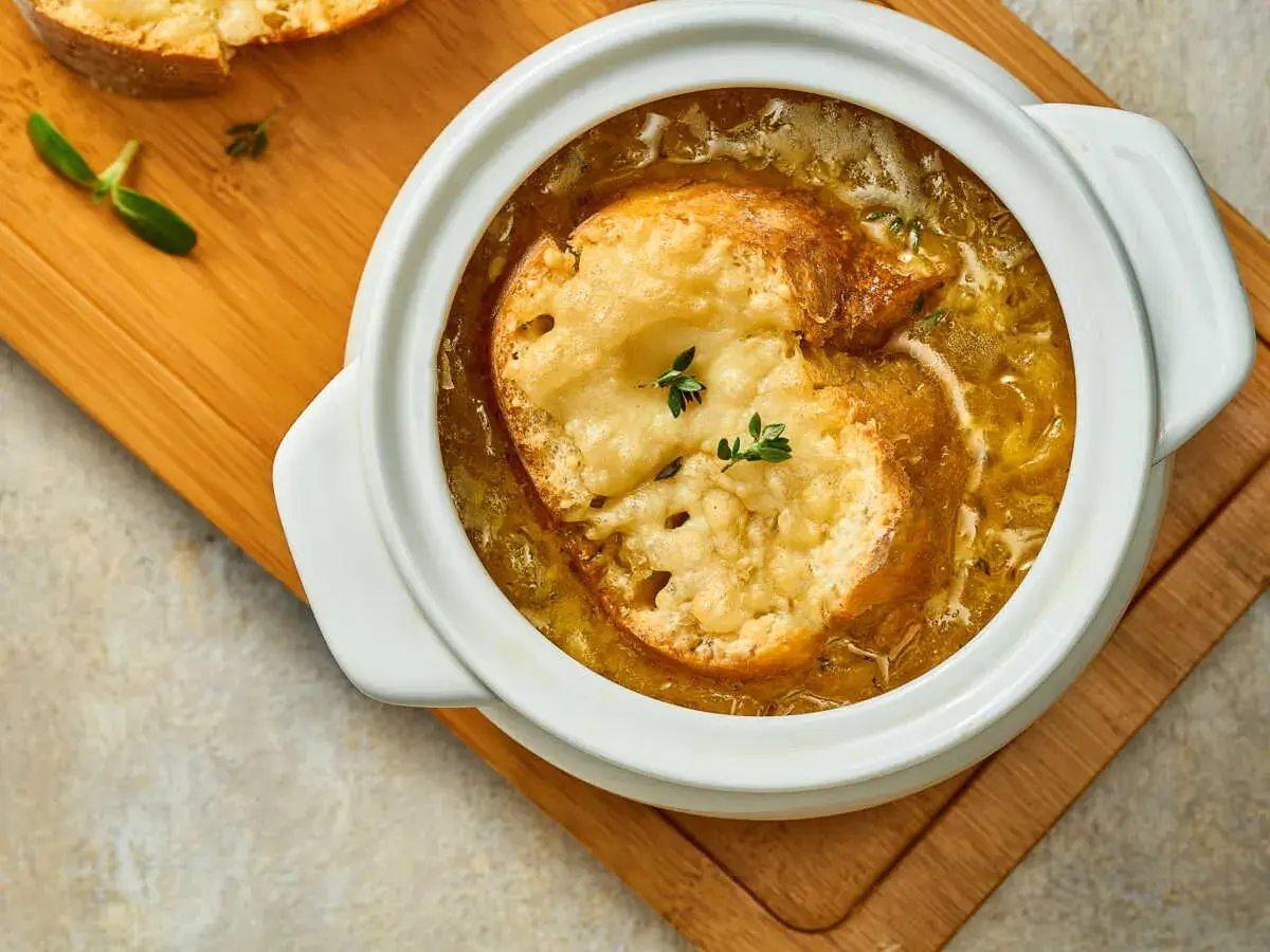 Soupe à l'oignon grand mère réconfortante, gratinée avec du pain et du fromage fondant, servie dans un bol blanc sur une planche en bois.