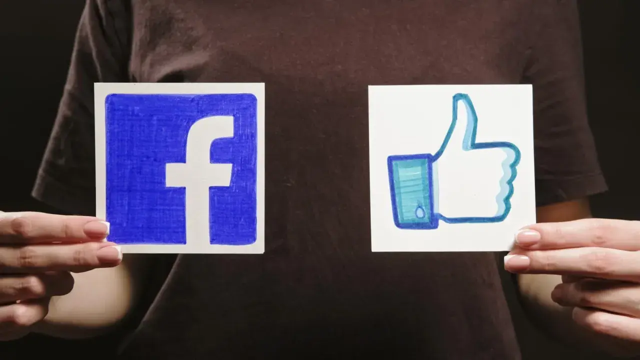 Dwie ręce trzymają kartki z logo Facebooka i kciukiem w górę.