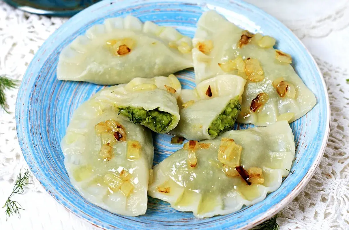 Pyszne pierogi z bobem, polane skwarkami z cebulki, na niebieskim talerzu.