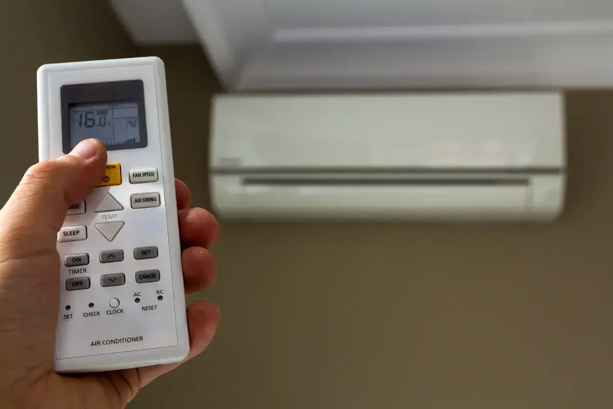 Mano che regola il telecomando del condizionatore, impostando la temperatura. Scopri quanto consuma un condizionatore per un comfort ottimale.