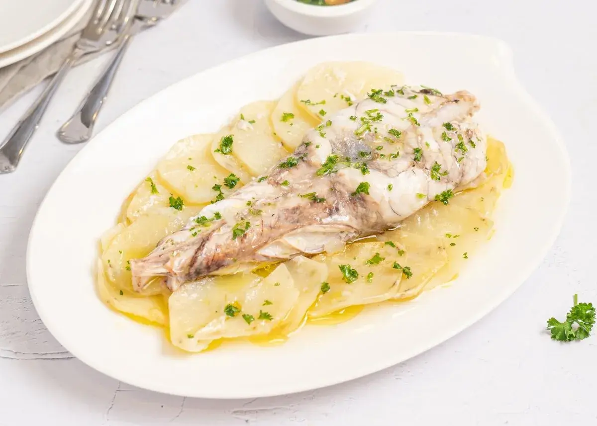 Rape al horno servido sobre patatas laminadas y espolvoreado con perejil fresco.