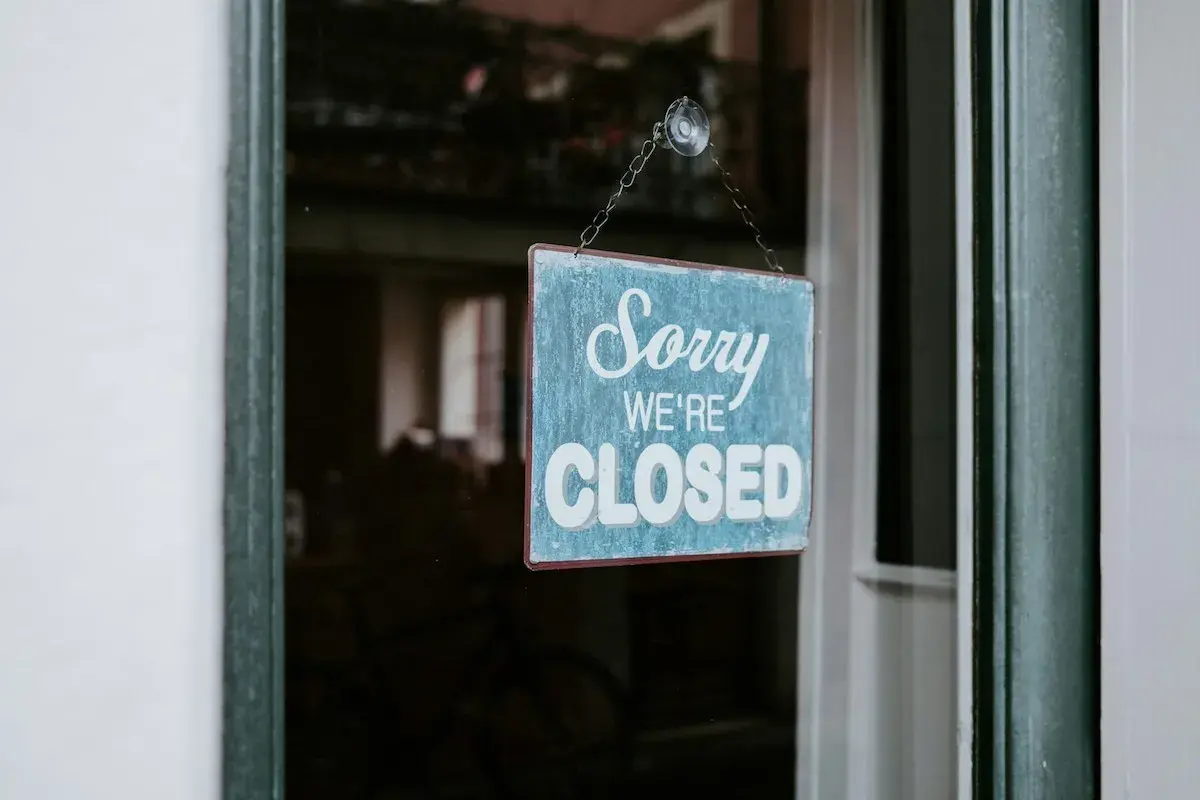 En blå skylt med texten "Sorry WE'RE CLOSED" hänger i ett fönster. Enskild firma i vilande.
