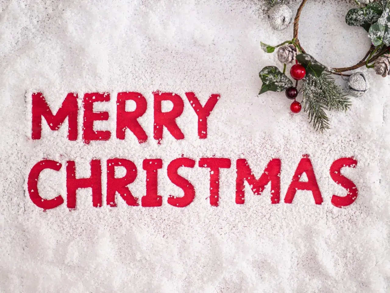 Lettere rosse su neve scrivono "Merry Christmas". Un festoso ramoscello natalizio con bacche e pigne completa la scena, evocando le classiche frasi natalizie in inglese.