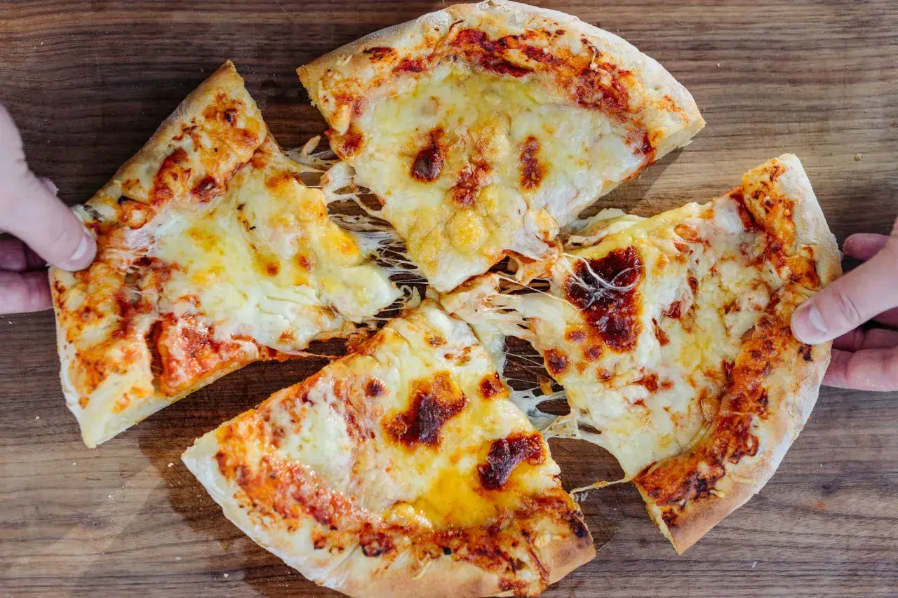 New York Style Pizza mit geschmolzenem Käse, von Händen gehalten, auf Holzuntergrund.