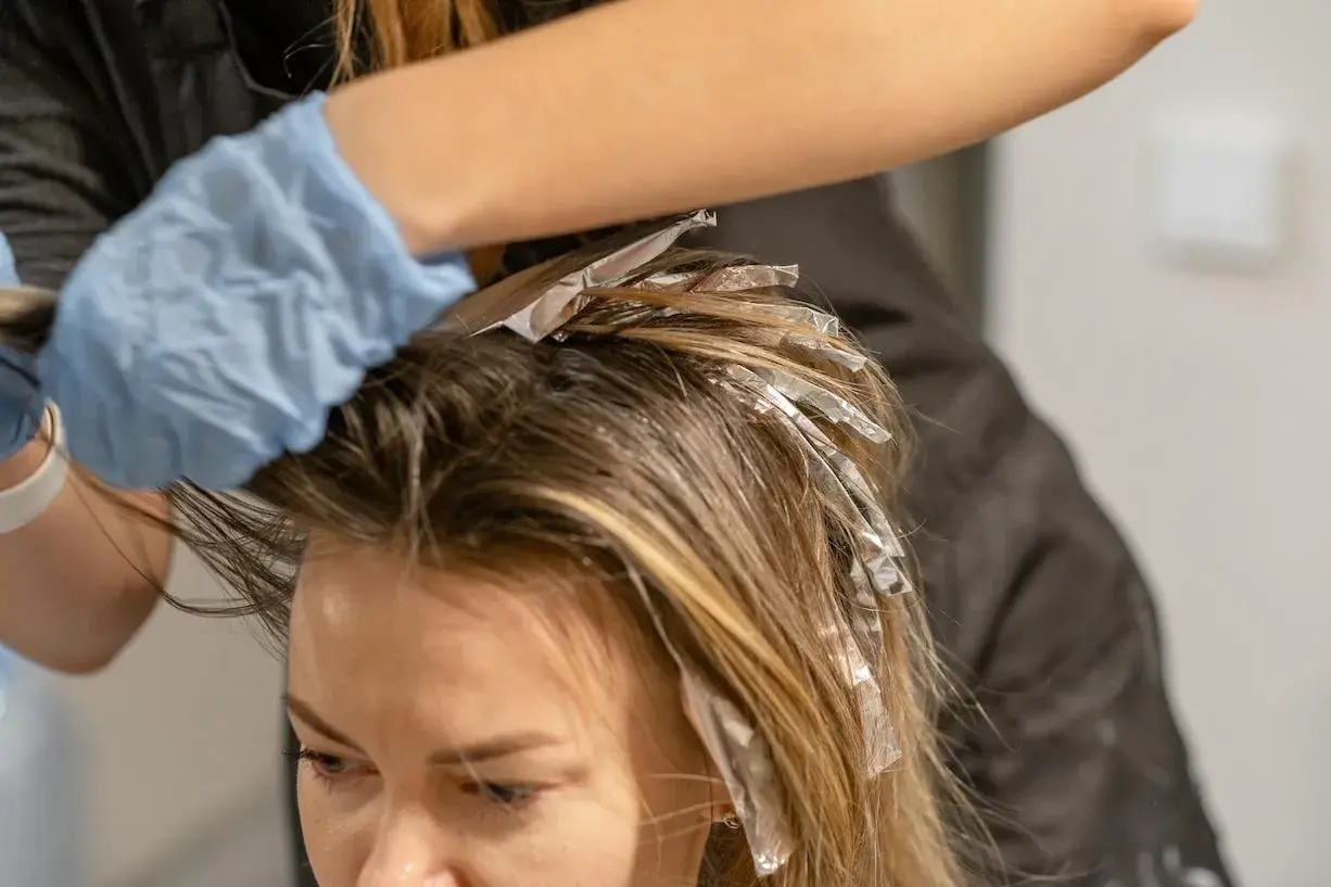 Manos enguantadas aplican mechas con papel de aluminio para un look face framing.