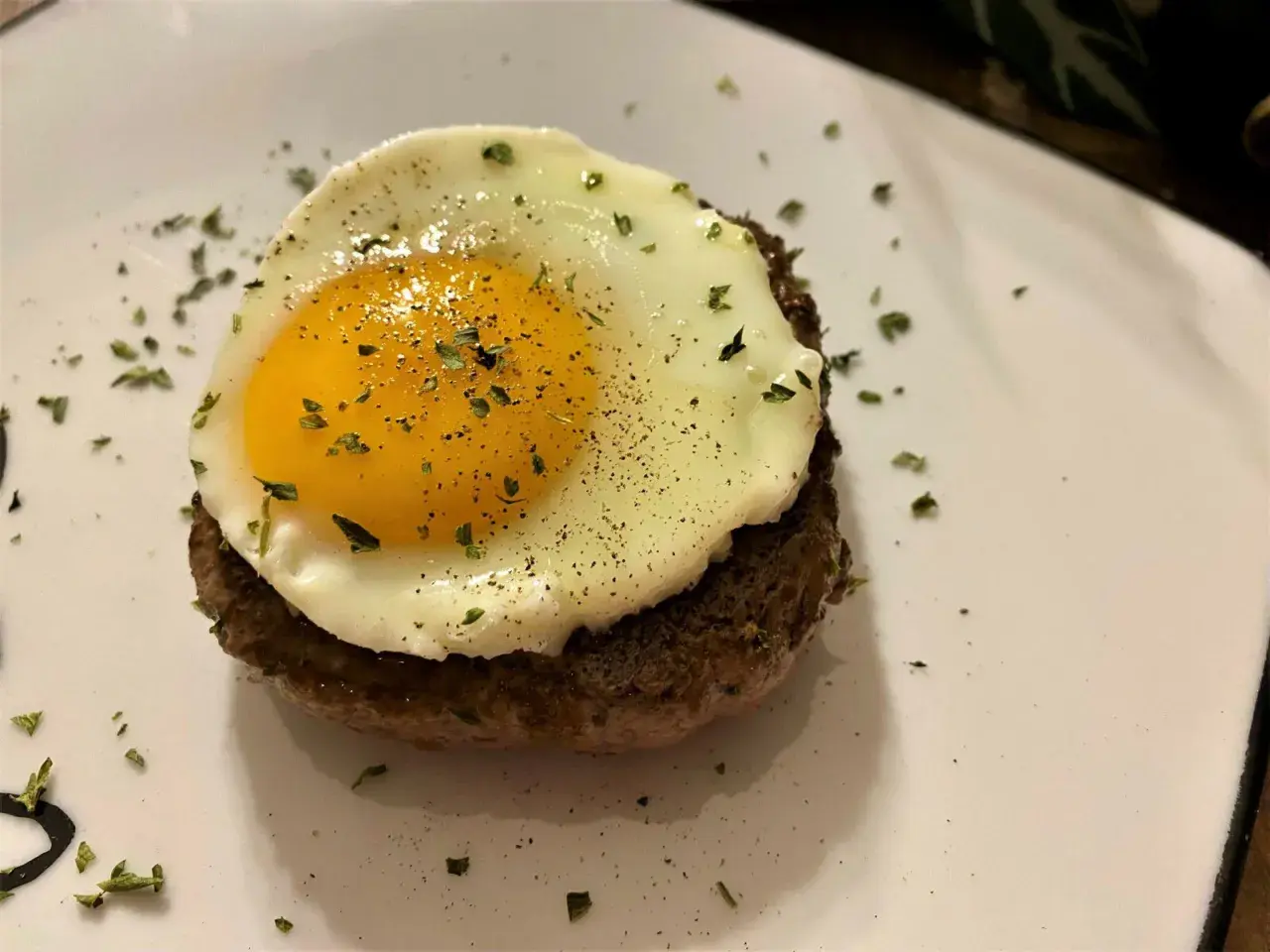 Un délicieux steak a cheval, un steak haché surmonté d'un œuf au plat, saupoudré d'herbes et de poivre.