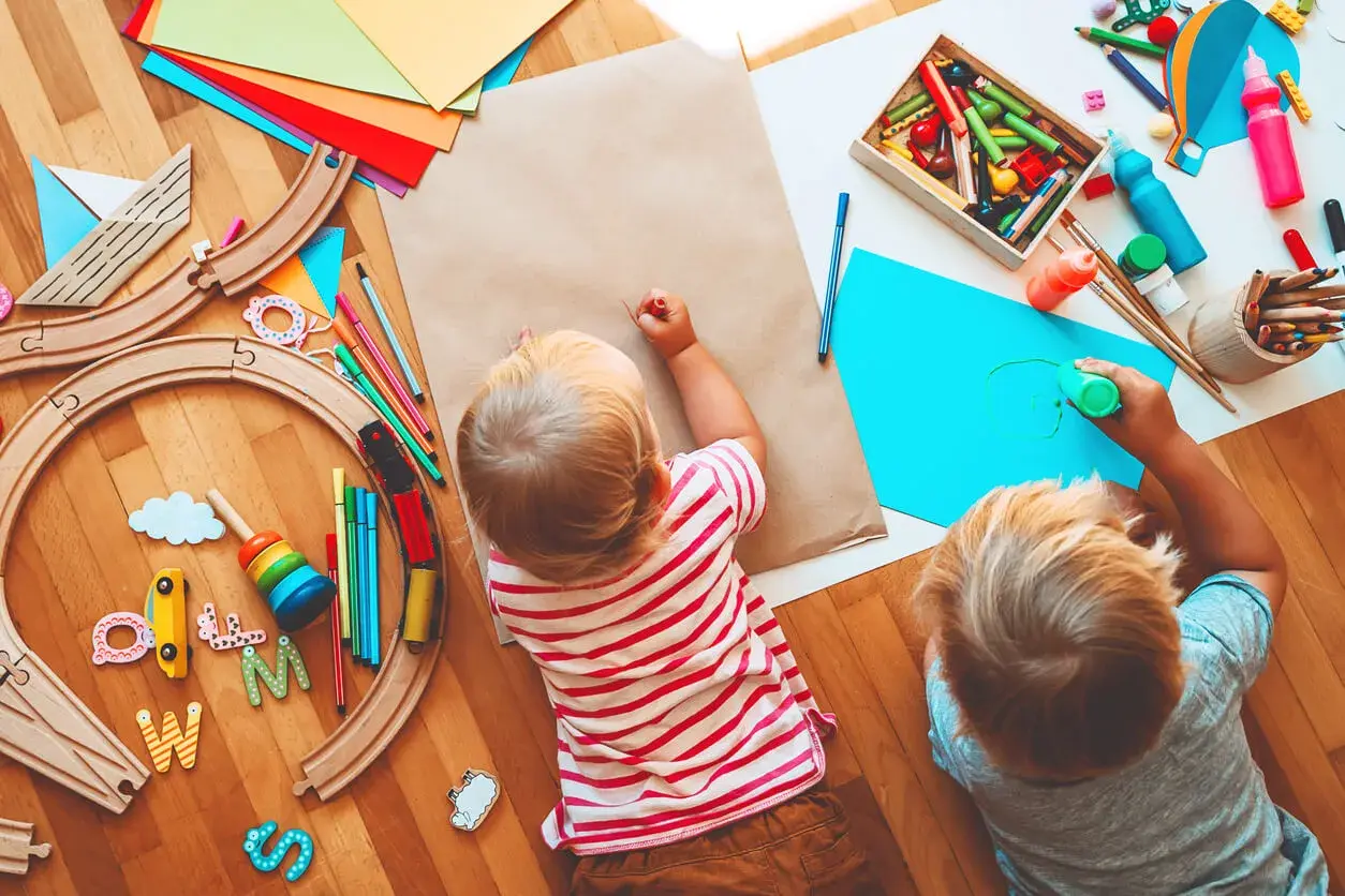 Dos niños pequeños disfrutan de actividades para niños de un año en guardería: pintan y juegan con un tren de madera.