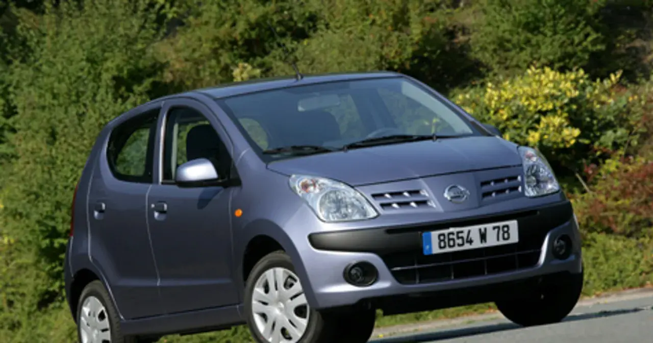 Niebieski Nissan Pixo z tablicą rejestracyjną 8654 W 78 zaparkowany na tle zieleni.