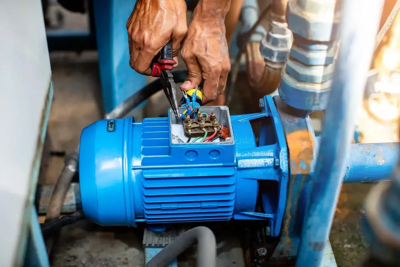 Manos trabajando en la caja de conexiones de un motor azul, revisando el cableado. El **vac significado** es crucial para el funcionamiento de esta bomba.