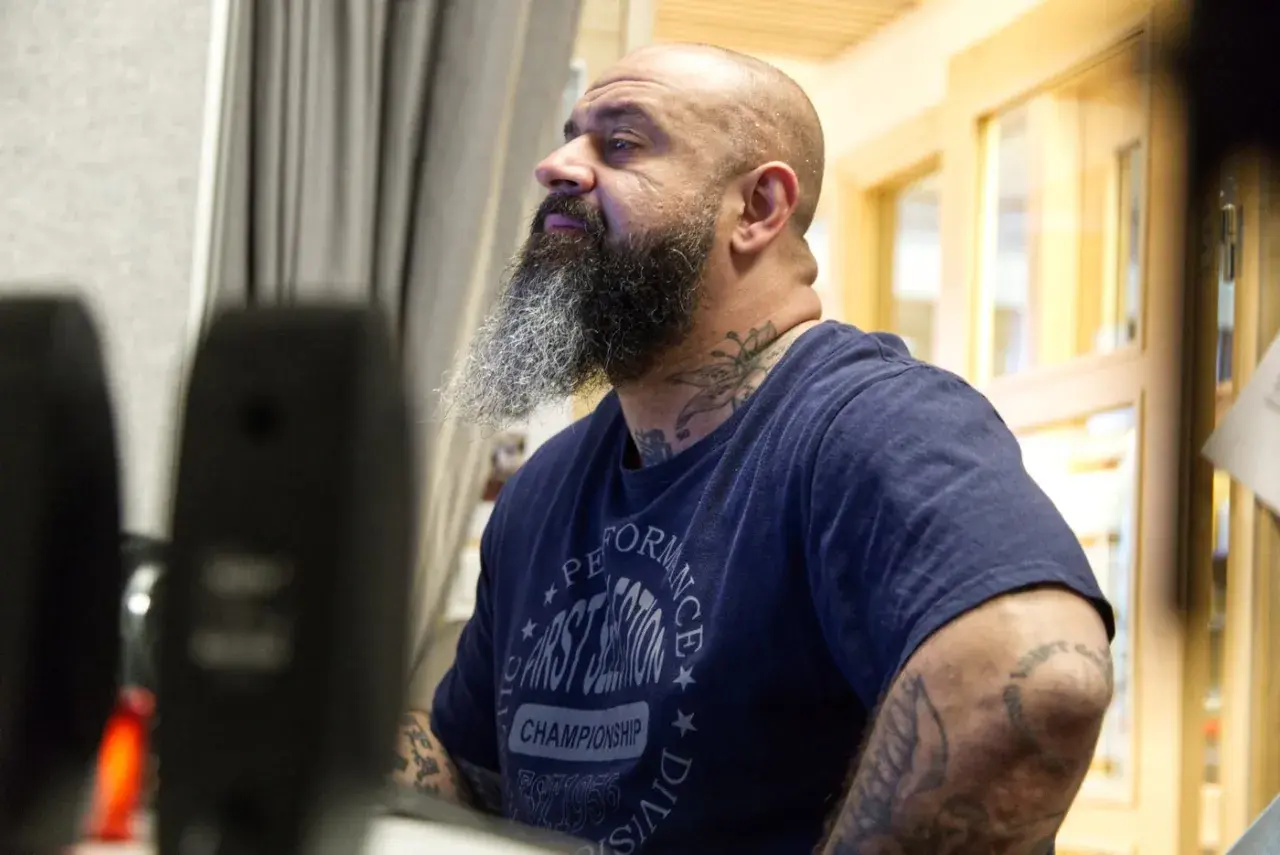 Man med skägg och tatueringar, klädd i en t-shirt med texten "Performance First Session Championship". Kanske en del av "kaka kartellen" som förbereder sig för något.