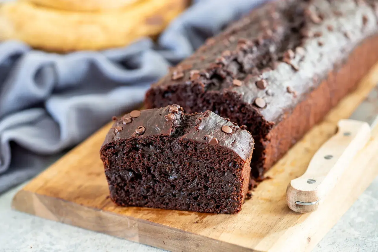 Fetta di banana al cioccolato, soffice e ricca, con gocce di cioccolato fondente, su tagliere di legno.