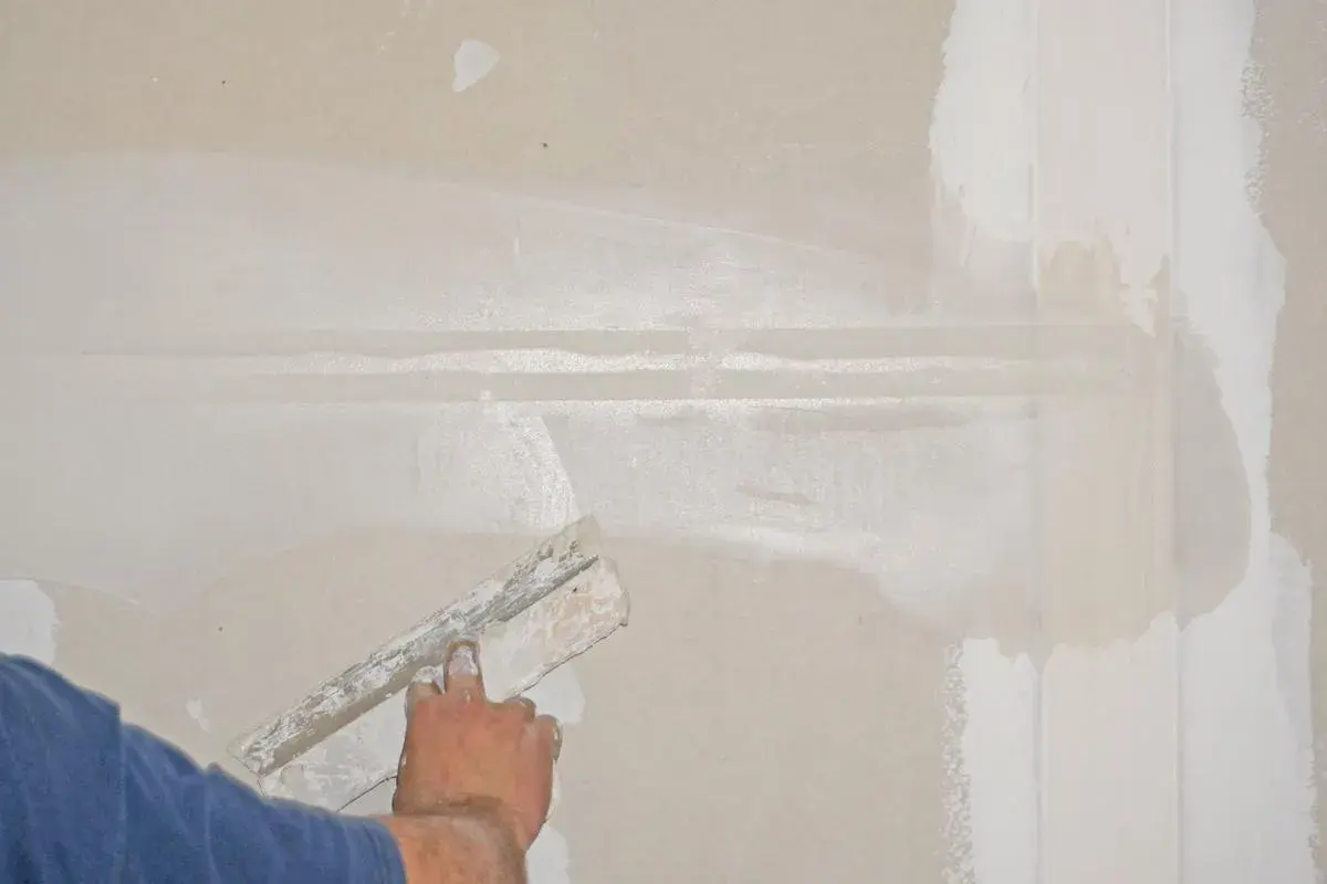 Hand spachtelt eine Rigips-Wand glatt. Die Naht wird mit Spachtelmasse bedeckt, um eine ebene Oberfläche für die weitere Bearbeitung zu schaffen.