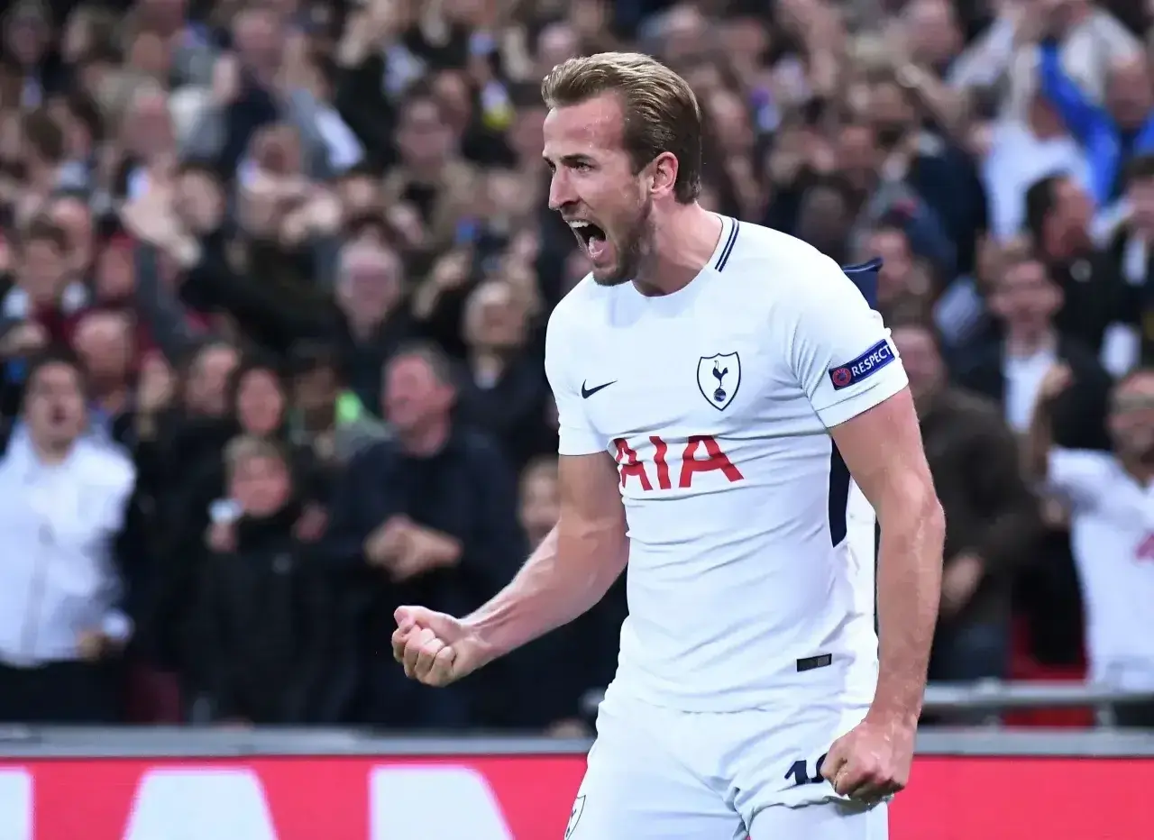 Harry Kane, jeden z najlepszych angielskich trenerów, świętuje bramkę. Tłum kibiców na trybunach.