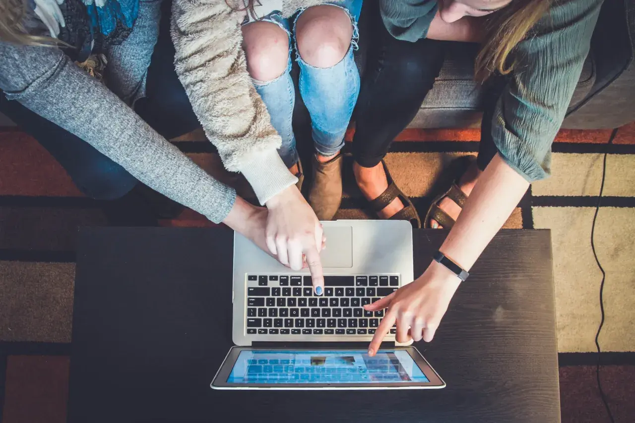 Flera personer pekar på en laptop och en surfplatta, ett tydligt exempel på delaktighet i ett projekt.