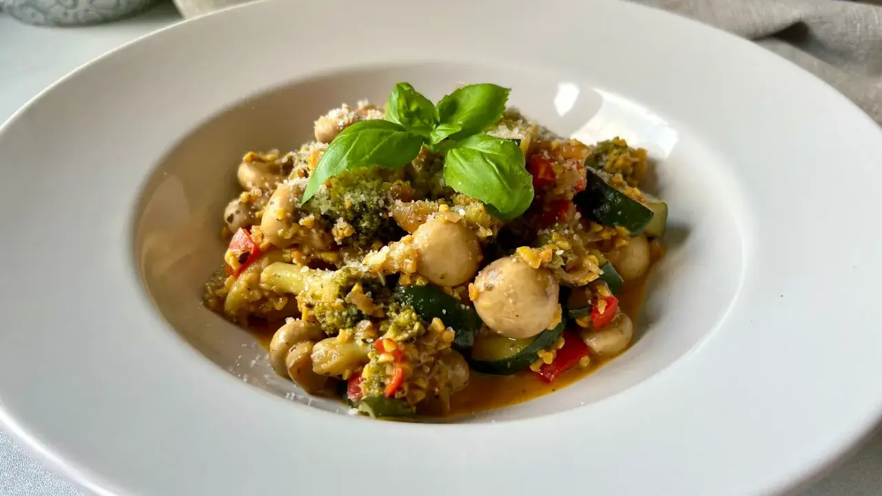 Pyszne kaszotto z warzywami: brokuły, cukinia, pieczarki i pomidorki, posypane parmezanem i udekorowane bazylią.