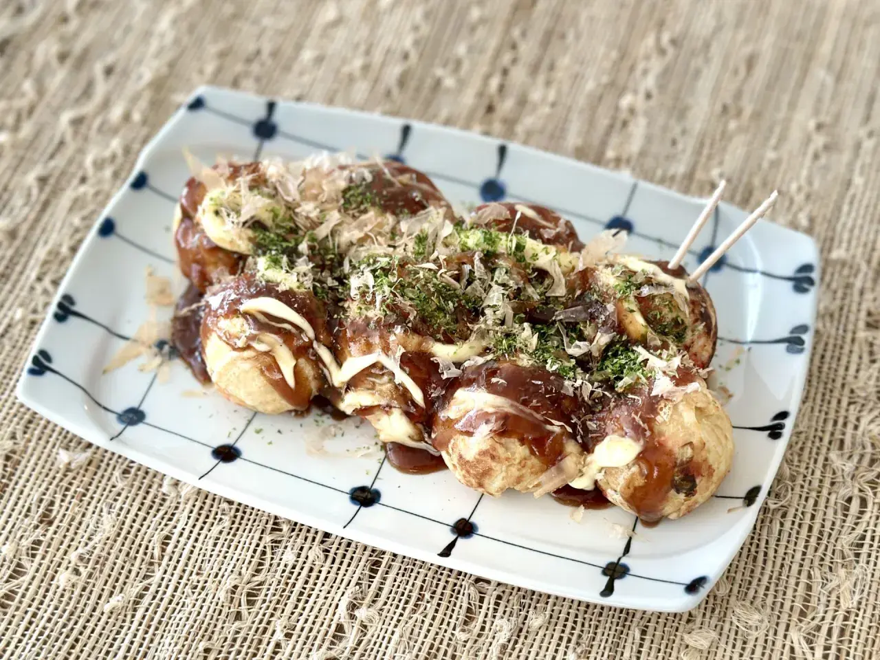 A plate of delicious takoyaki food, drizzled with sauce and mayonnaise, topped with bonito flakes and parsley.