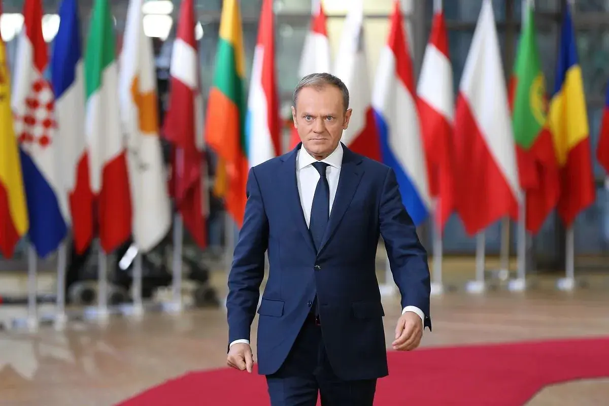 Donald Tusk, z niemieckim pochodzeniem, idzie na tle flag UE.