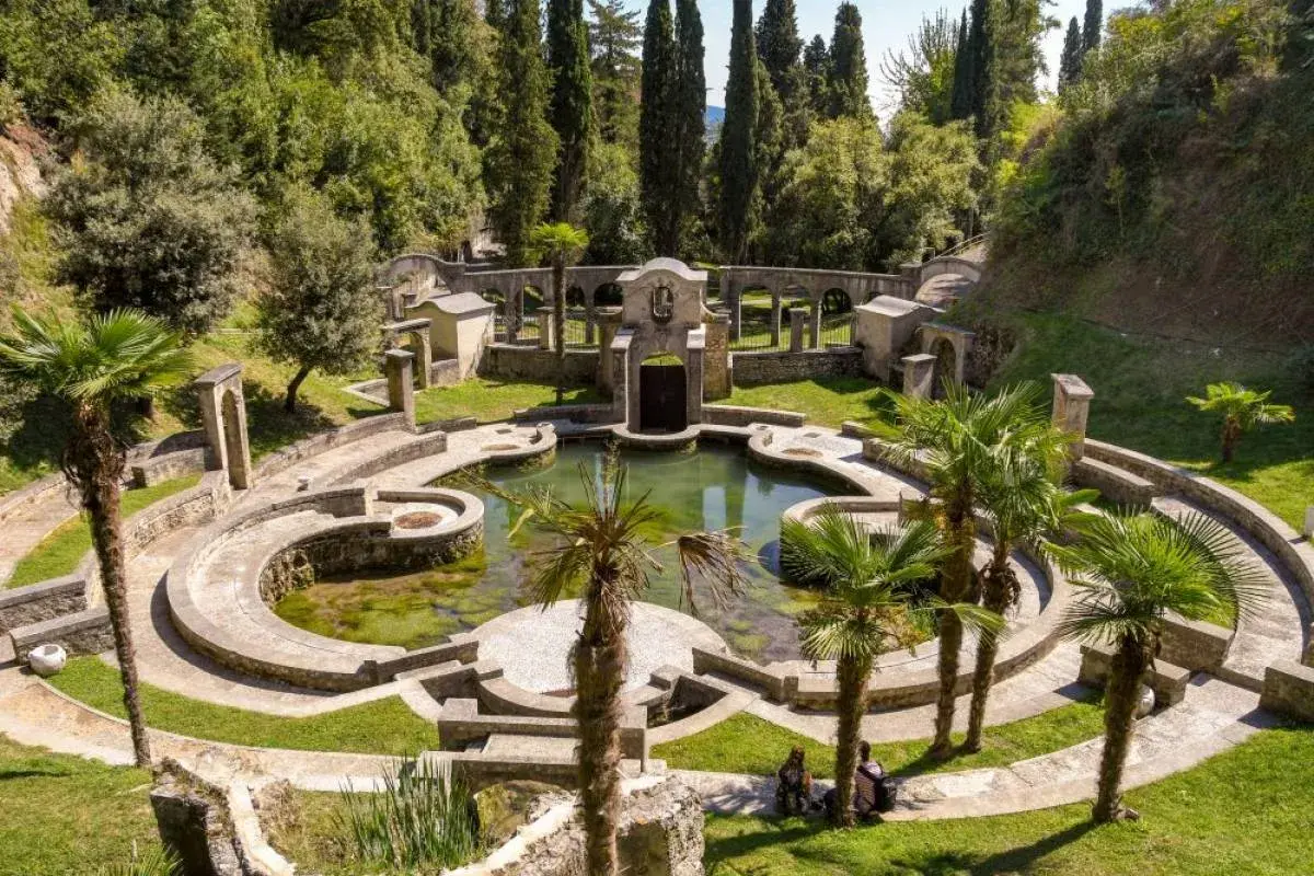Un incantevole giardino botanico sul Lago di Garda, con un laghetto circondato da architetture in pietra e palme.